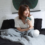 Woman sitting in bed with a weighted blanket on her lap and holding a coffee cup