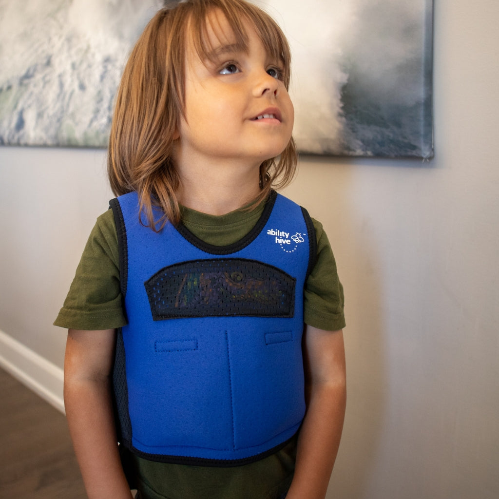 Child wearing a blue weighted compression vest with a visible brand logo indoors.